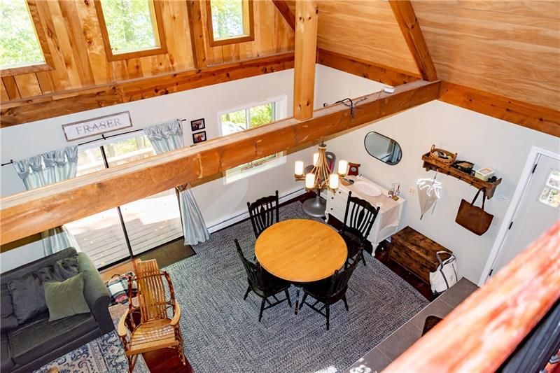 Overhead view of a dining area with round table, black chairs, and a small sofa. Natural wood beams and windows are visible.