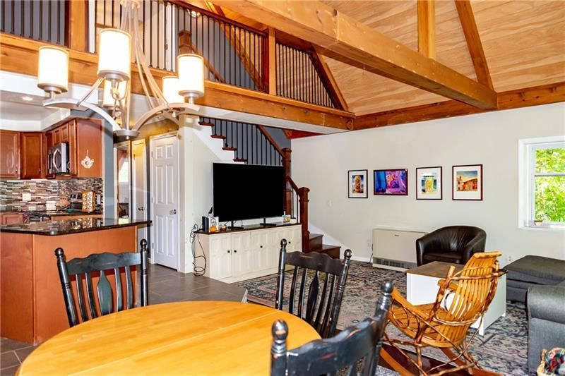 Living room with open kitchen, exposed beams, staircase, and art.