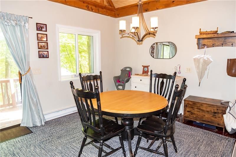 Dining room with round table and black chairs, baby seat, window, chandelier, and a rug.