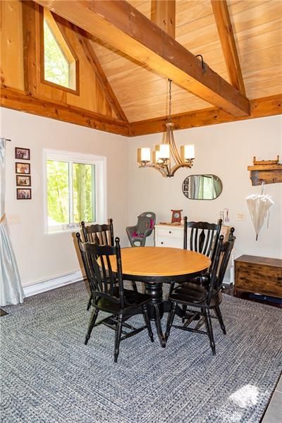 Dining room with round table, black chairs, chandelier, and a vaulted, wood-beam ceiling.