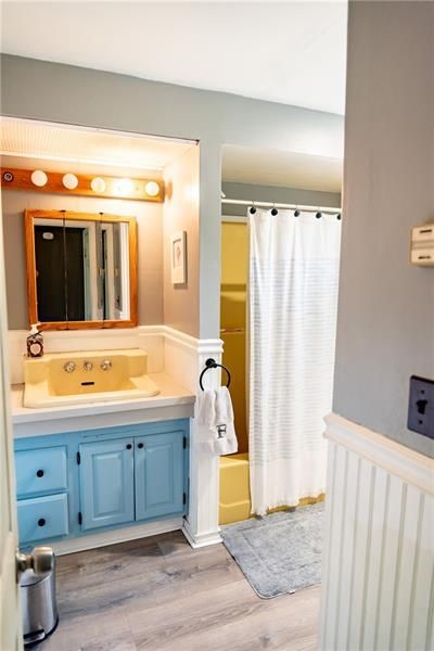 Bathroom with yellow vanity, blue cabinets, and a yellow shower. Light gray walls, white shower curtain.
