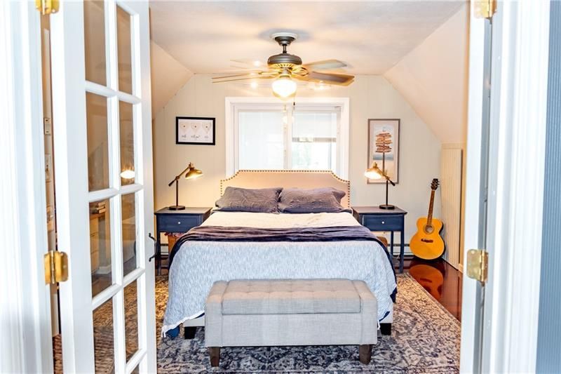 Bedroom interior: bed centered, nightstands, guitar, french doors, tan walls, light ceiling fan.