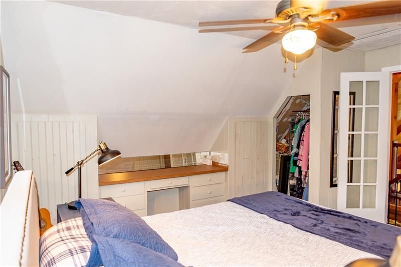 Bedroom with bed, desk, closet, and ceiling fan. White walls, blue bedding, light wood accents.