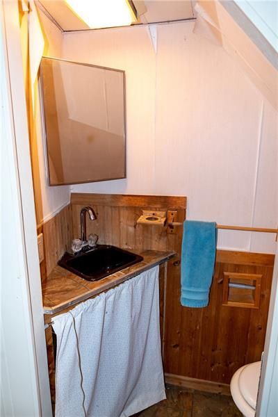 Small bathroom with wooden paneling, black sink, mirror, and white curtain under the sink. A blue towel hangs on the wall.
