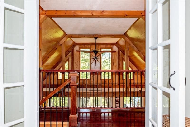Interior view of a wooden cabin loft with a railing, dark floor, and open French doors.