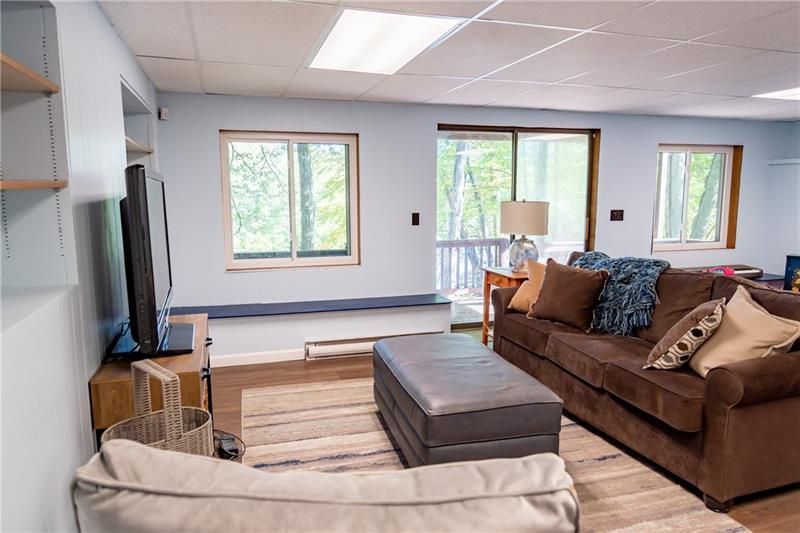 Living room with brown sofa, ottoman, and windows overlooking a wooded area.