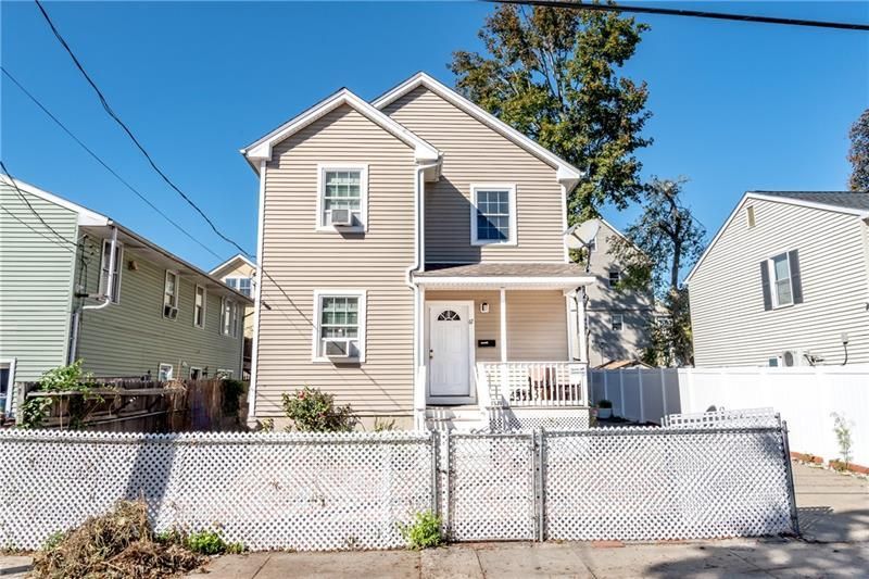 Two-story beige house with white trim, porch, and a white picket fence under a blue sky.