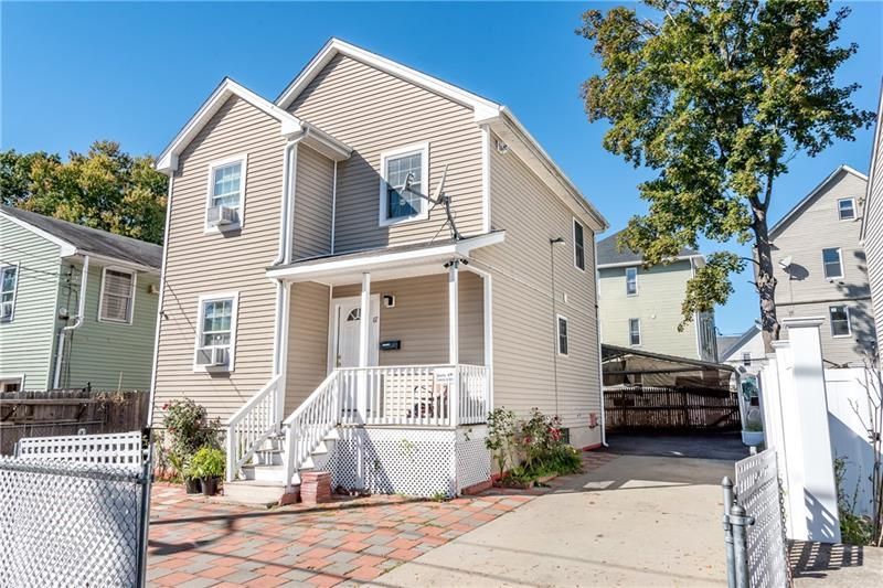 Beige two-story house with white porch and stairs, brick walkway, and driveway on sunny day.