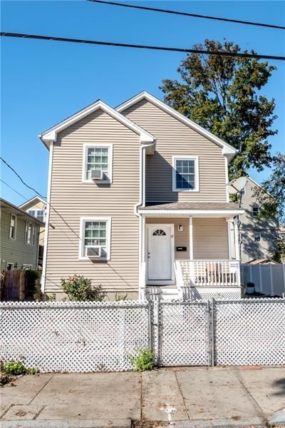 Two-story house with beige siding, white trim, and a small porch behind a white picket fence on a sunny day.