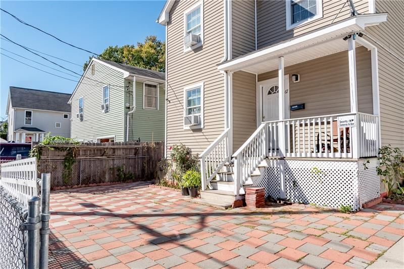 Two-story house with a porch and brick driveway on a sunny day.