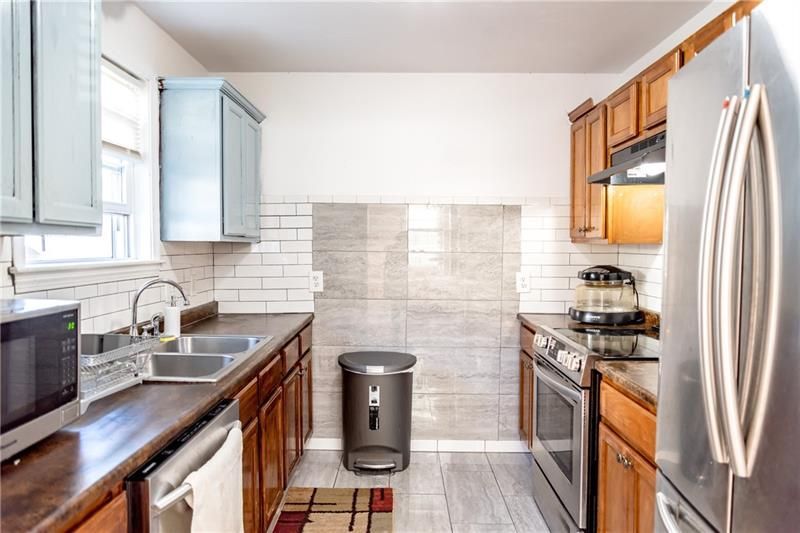 Small kitchen with wooden cabinets, stainless steel appliances, and white tile backsplash.