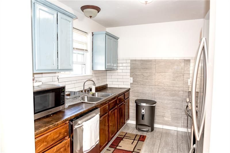 Kitchen with light blue upper cabinets, dark wood lower cabinets, stainless steel appliances, and a gray-toned tiled backsplash.