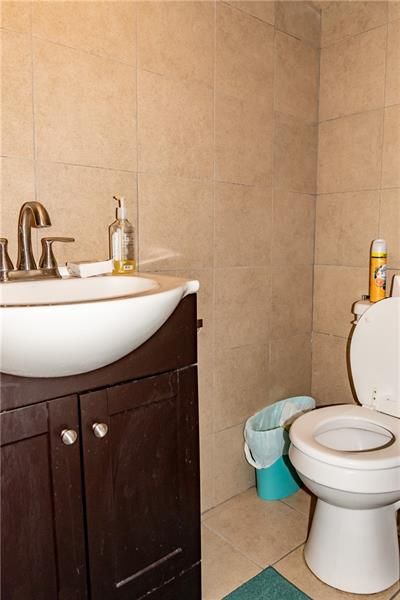Bathroom with white sink, dark brown cabinet, and a toilet. Beige tile walls.