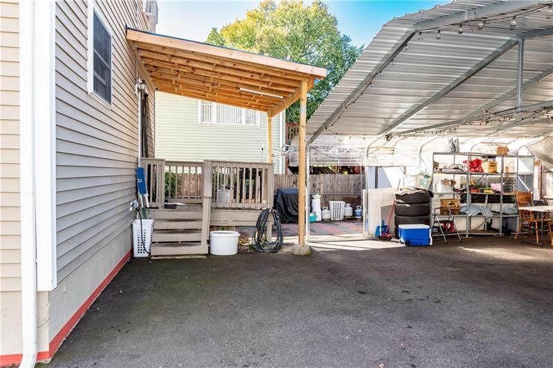 Asphalt driveway with a wooden porch and attached carport. Exterior of a light-colored house visible.