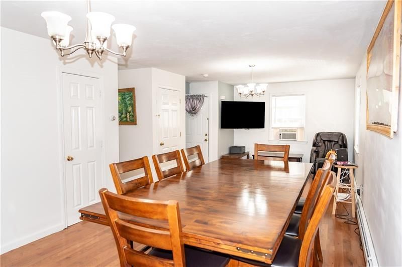 Dining room with large wooden table and chairs, hardwood floor, white walls, and TV.