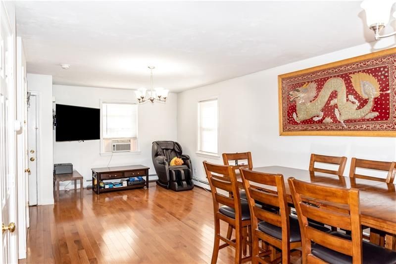 A living/dining room with hardwood floors, a large table with chairs, a massage chair, and a mounted TV.