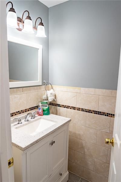 Bathroom with white vanity, tan tiled wall, blue wall, and mirror.