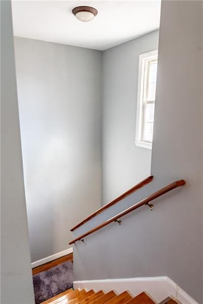 Stairwell with wooden steps and handrails; gray walls, small window, ceiling light.