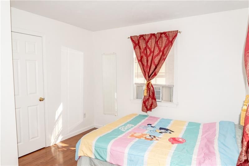 Bedroom with a bed, window, door, and a full-length mirror. A red curtain is tied back.