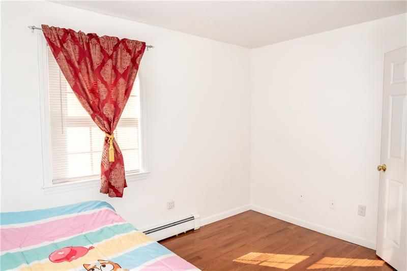 Empty bedroom with a window, red curtain, bed, and hardwood floor.