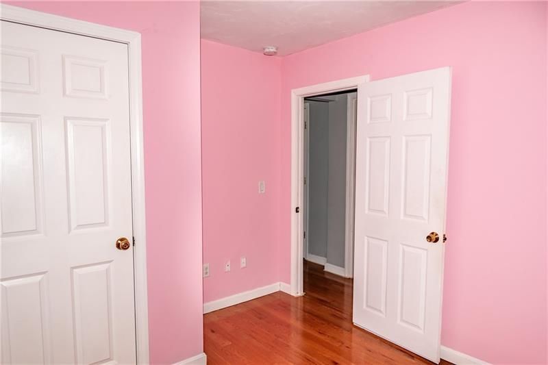 Empty pink bedroom with white doors and hardwood floors.