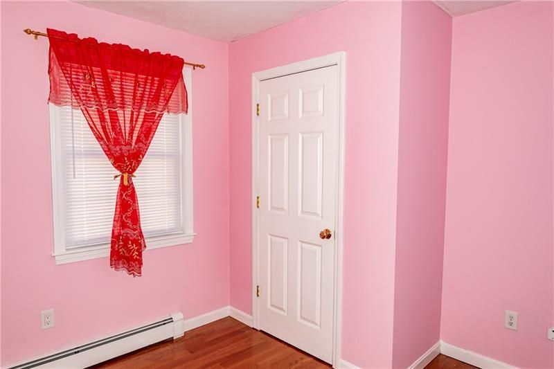 Pink bedroom with red curtain over a window and white door.