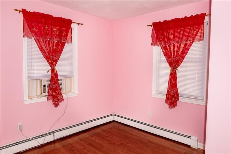 Pink-painted room with two windows, each with a red curtain. An air conditioner is in one window.
