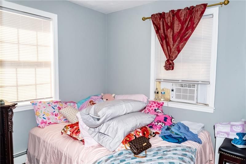 Bedroom with unmade bed, light blue walls, two windows, and red curtain.