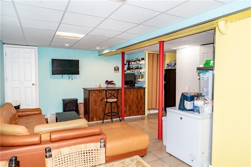 Basement with bar, seating, and a TV. Blue, yellow, red and brown hues are used. There is a fridge and a white door present.