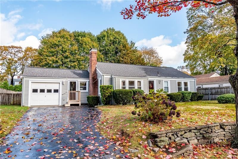 Ranch-style house with attached garage, wet driveway with fallen leaves, and autumn trees.