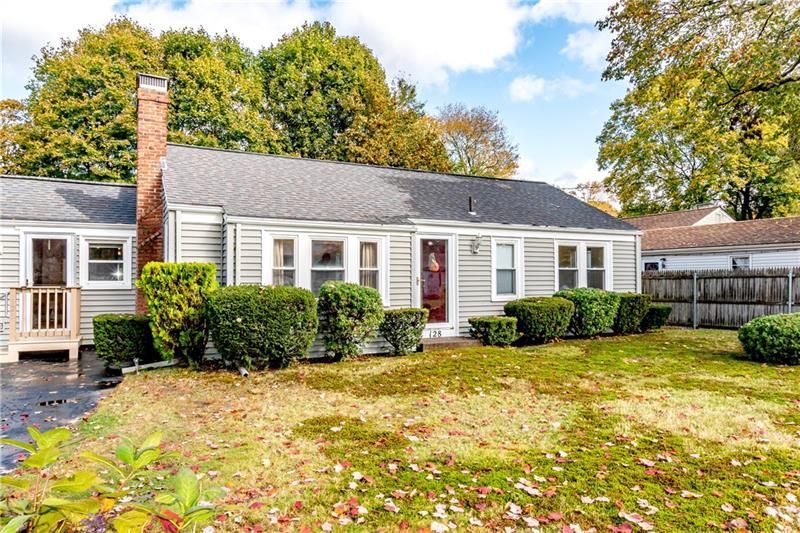 A small, single-story house with gray siding, a brick chimney, and a brown front door.