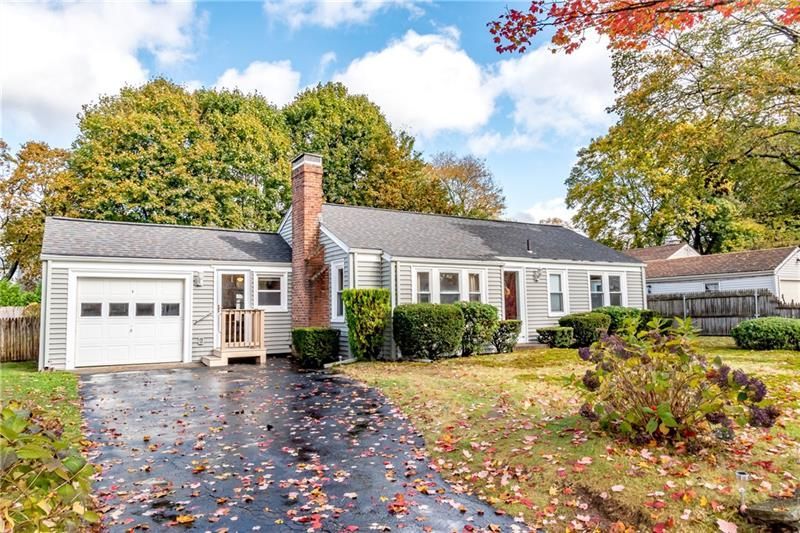 Gray ranch-style house with attached garage, chimney, and fall foliage in yard. Asphalt driveway.