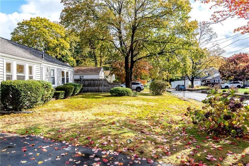 A suburban house with a grassy lawn and autumn trees. Sunlight and fallen leaves.