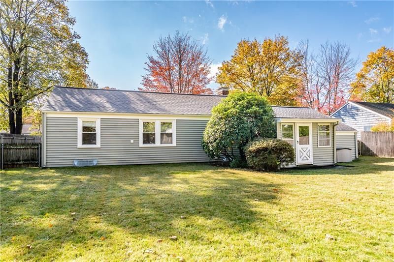 Back of a gray house with a small porch, green lawn, and autumn trees under a blue sky.