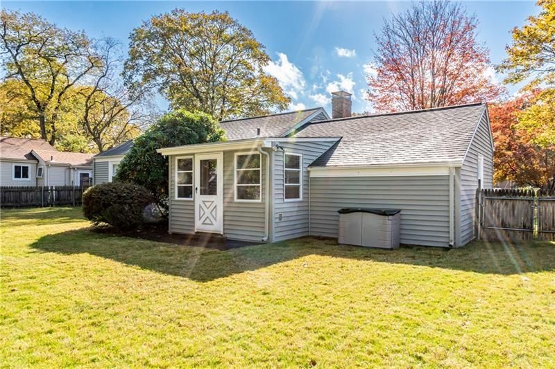 Back view of a light gray house with a small sunroom and a yard.