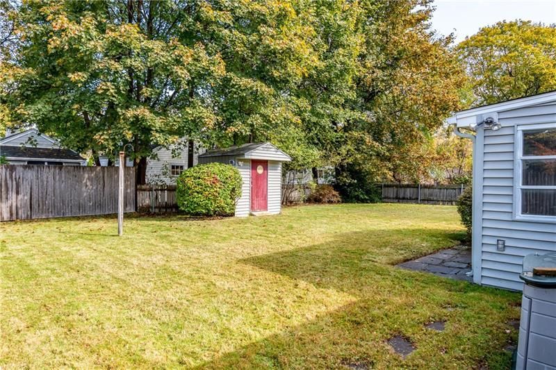 Backyard with shed, trees, and partial house view; sunny day with green grass.