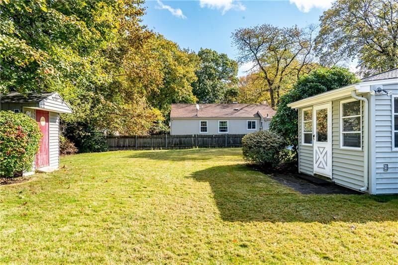 Backyard with green grass, shed on the left, small house on the right, and trees in the background.
