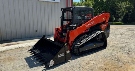 A skid steer is parked in a gravel lot in front of a building.