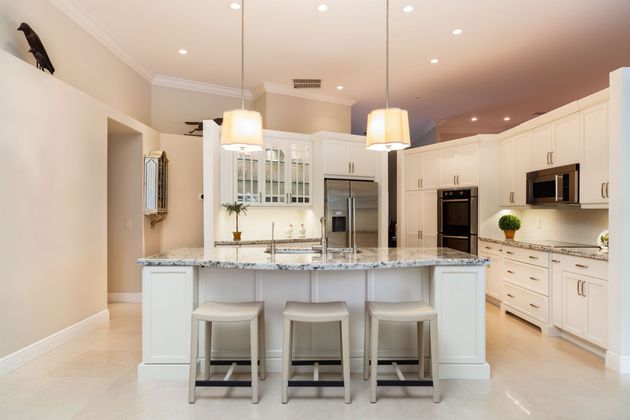 A bright kitchen featuring white cabinets, a large granite island with three stools, and two pendant lights overhead.