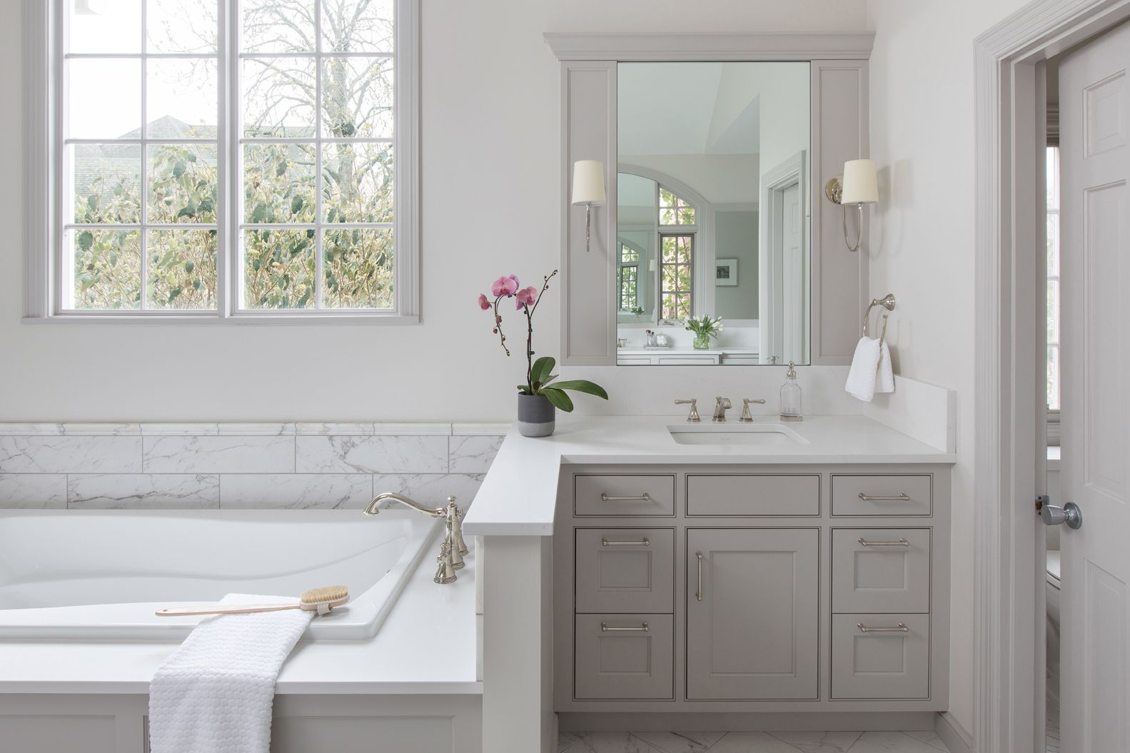 Bright white bathroom with a bathtub, vanity, mirror, and window light