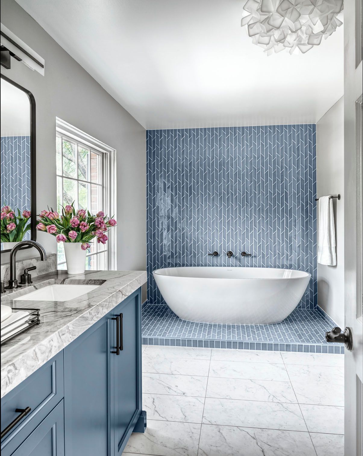 Bright modern bathroom with blue vanity, marble countertop, freestanding tub, and blue tile shower wall