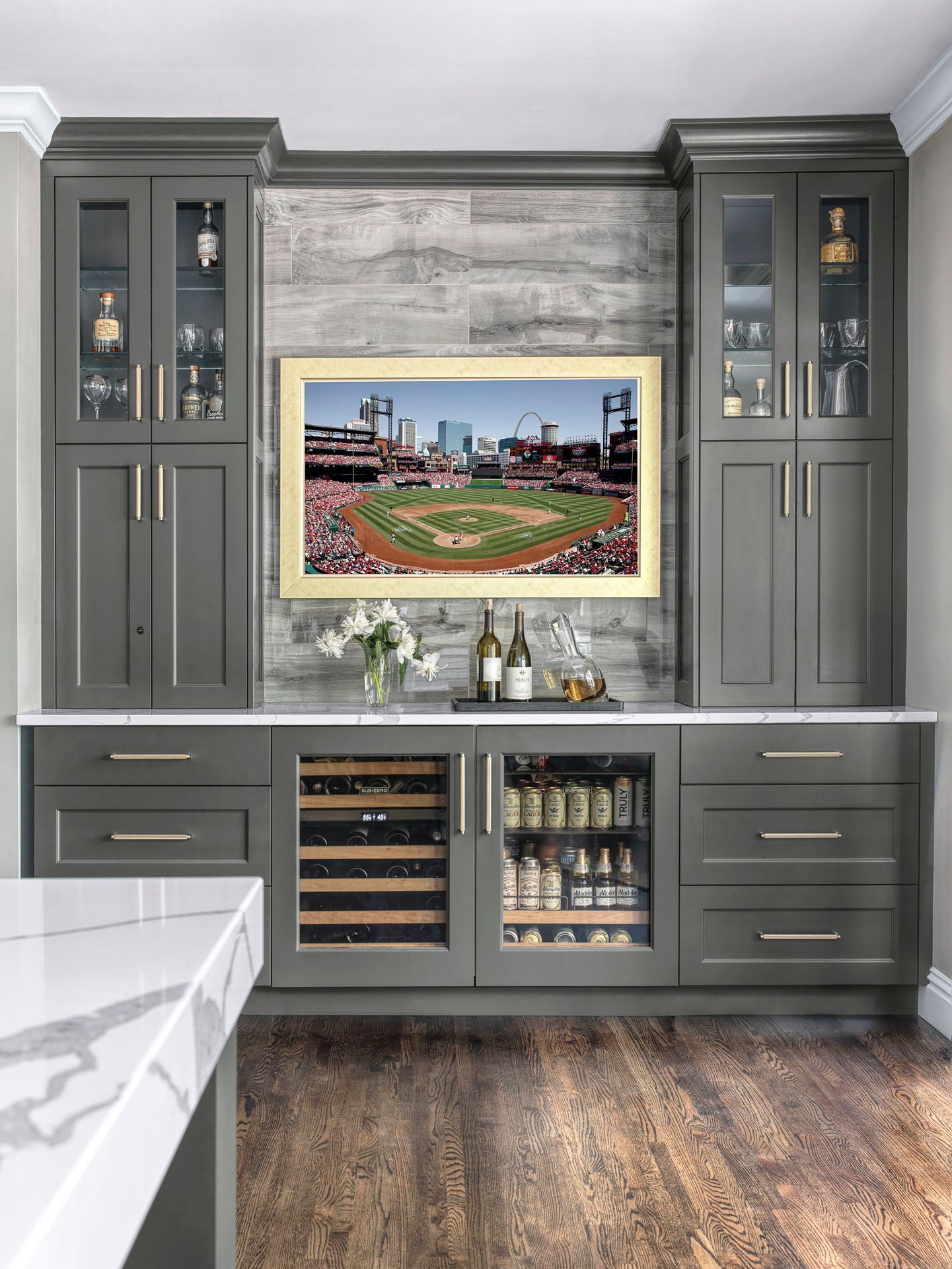 Gray built-in kitchen cabinet with beverage fridge and TV above the counter