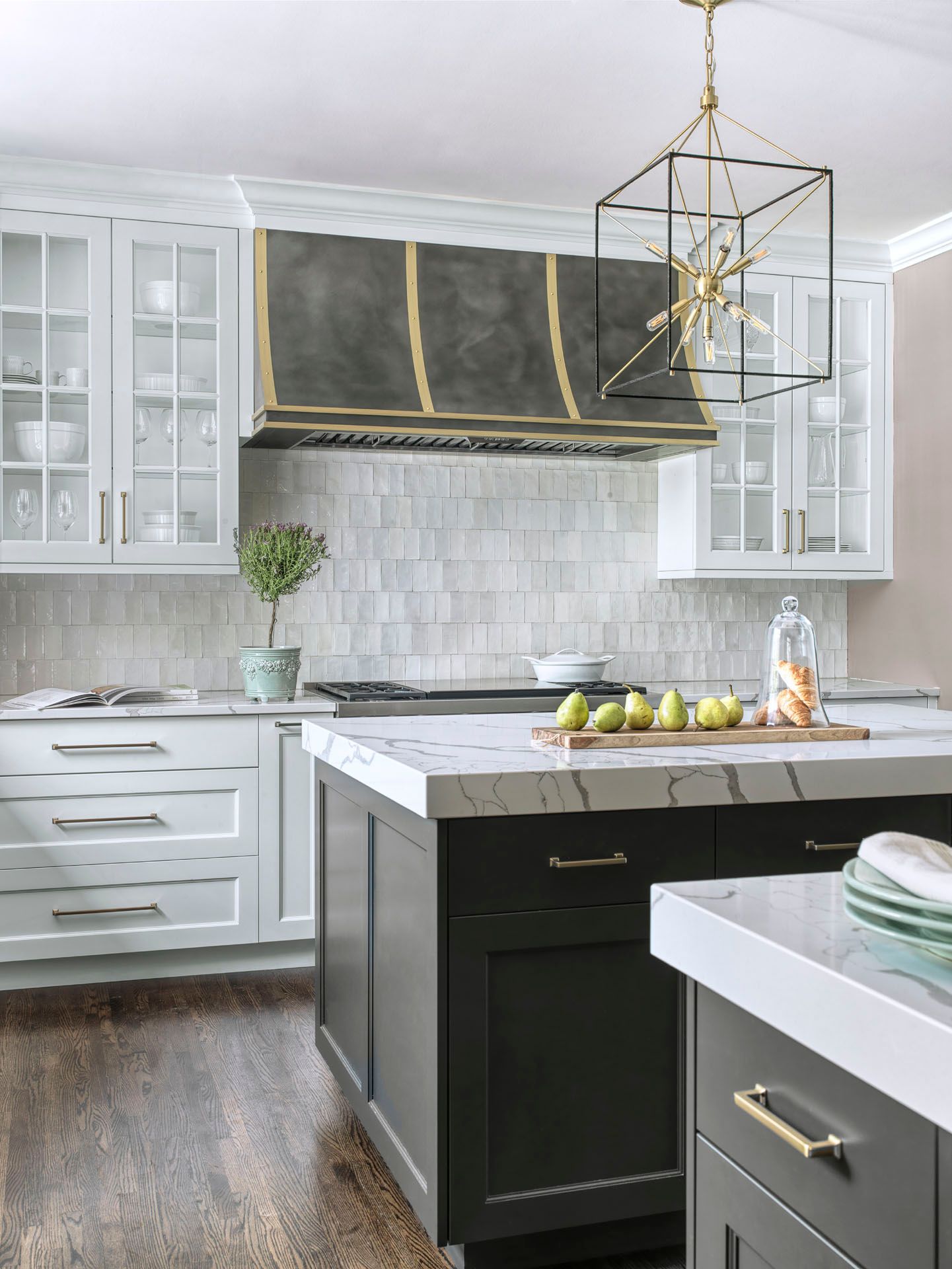 Bright modern kitchen with white cabinets, black island, marble countertops, and gold pendant light