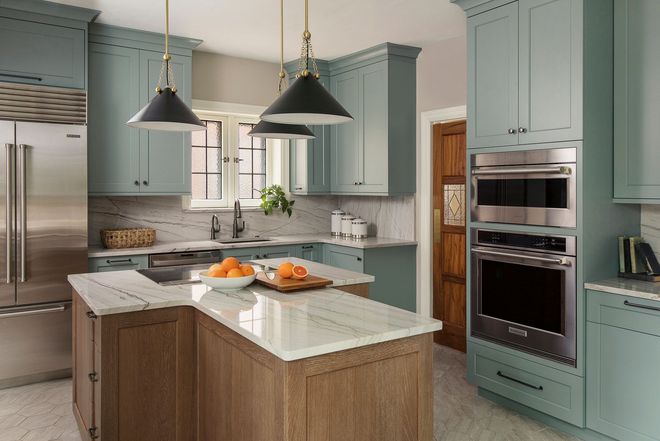 Modern kitchen with teal cabinets, stainless appliances, marble island, and black pendant lights