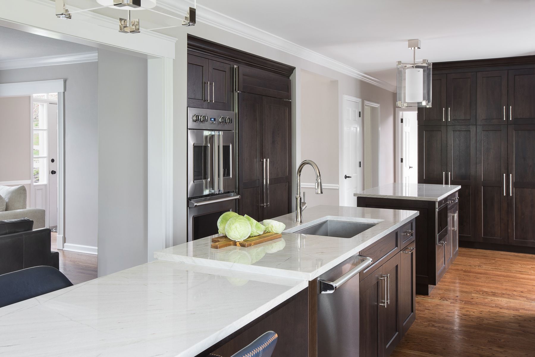 Modern kitchen with white island, dark cabinets, stainless appliances, and wood flooring.