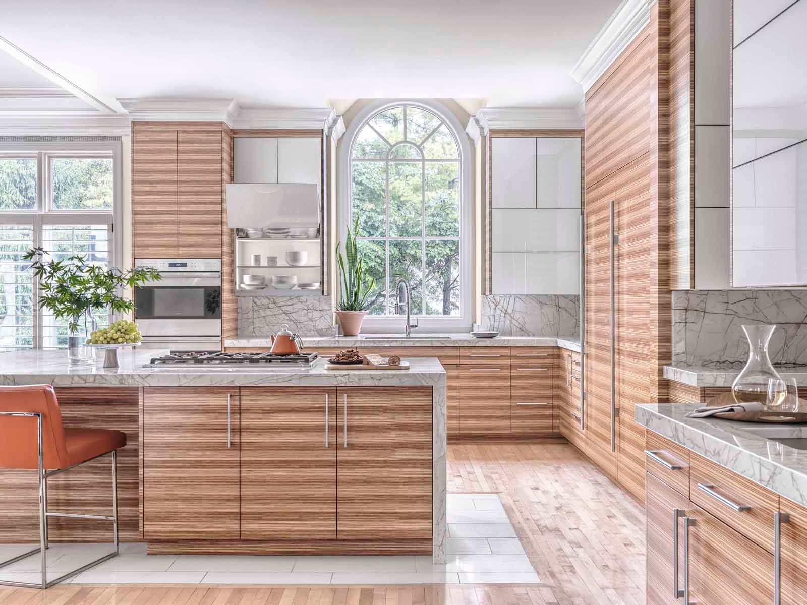 Bright modern kitchen with wood cabinets, marble countertops, island seating, and large arched window