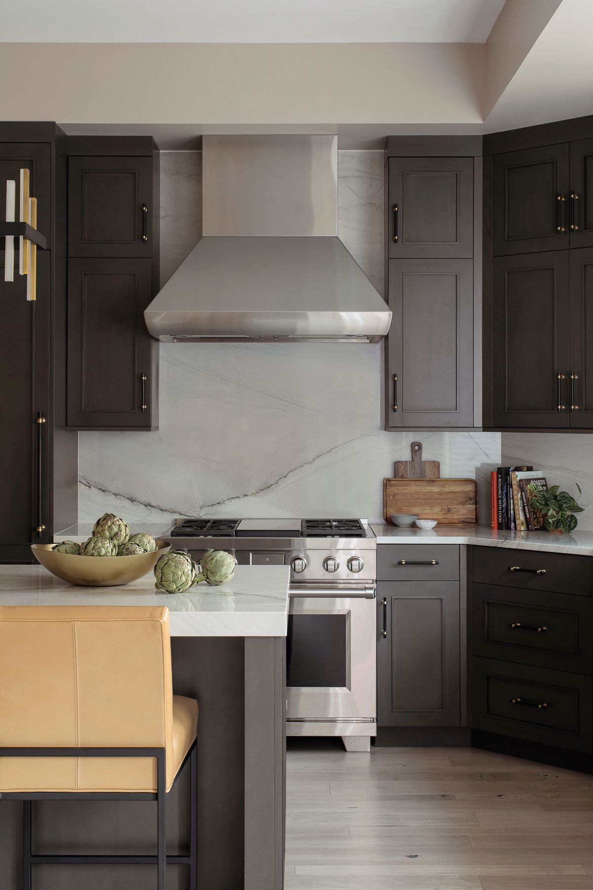 Modern kitchen with dark cabinets, marble backsplash, stainless stove, and a central island with stools.