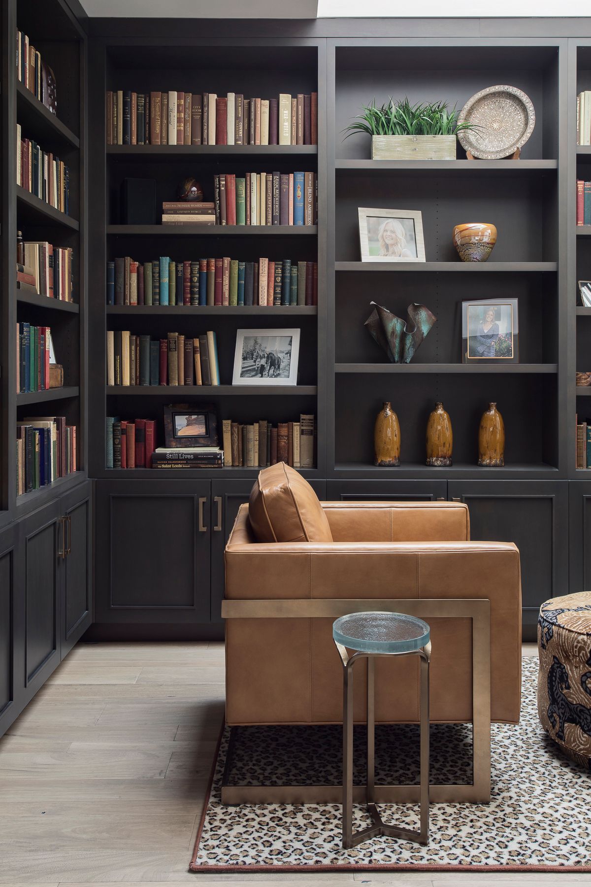 Cozy library nook with dark bookshelves, tan armchair, and small stool on a patterned rug.