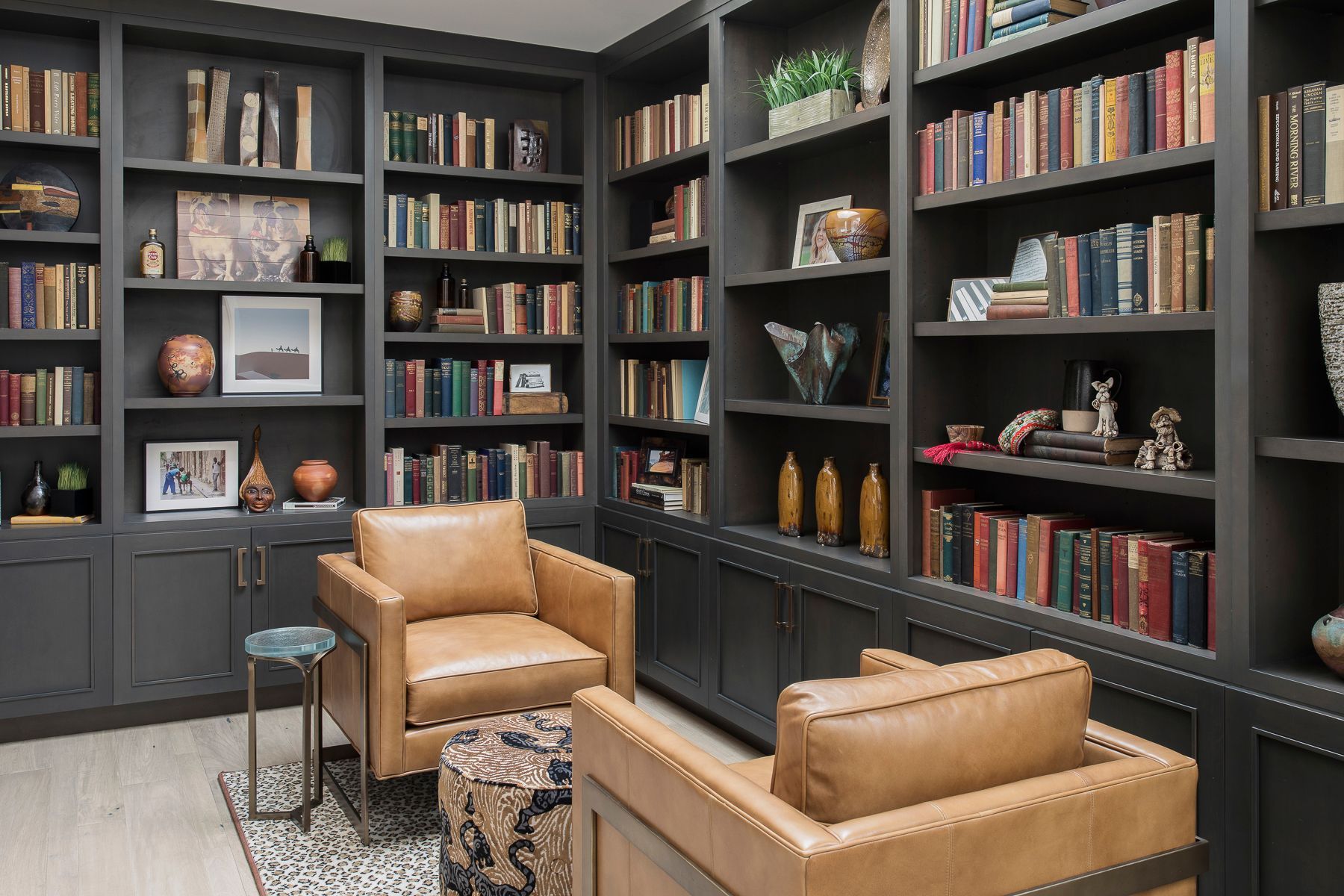 Modern home library with dark built-in shelves, leather chairs, books, and decorative objects