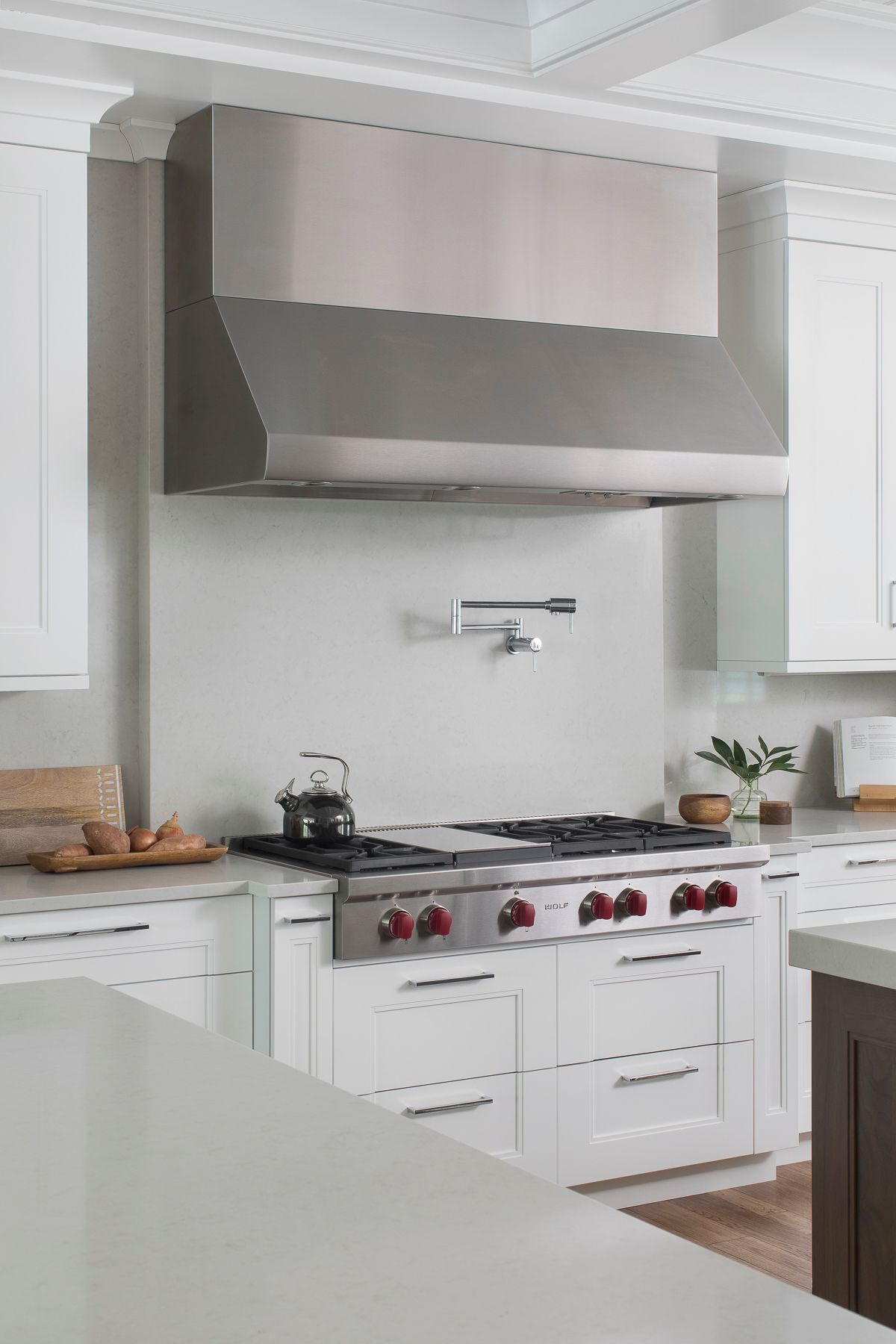 Modern white kitchen with stainless steel range hood and gas stove under a marble backsplash.